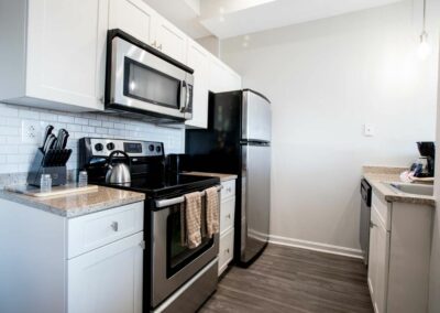 Galley style kitchen with hardwood style floors and stainless steel appliances in The Pepper Building apartments